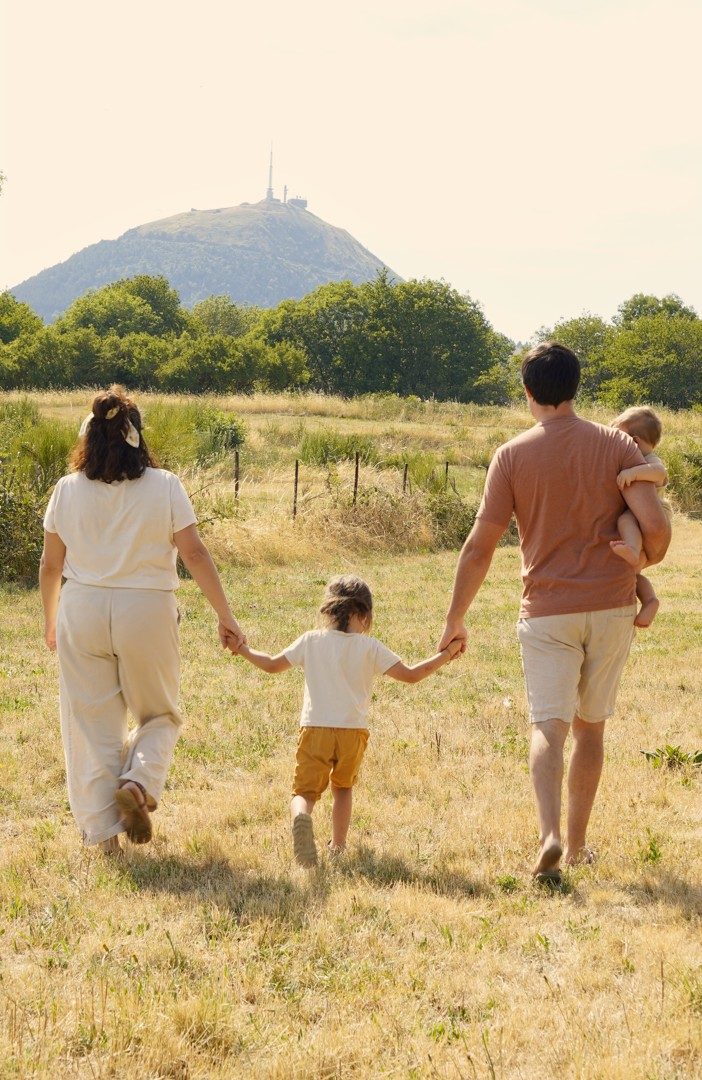La famille de dos, main dans la main, marchant dans un pré vers le puy de Dôme